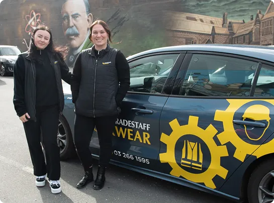 Two Tradestaff Workwear team members standing beside a branded company vehicle featuring the yellow Tradestaff Workwear logo.